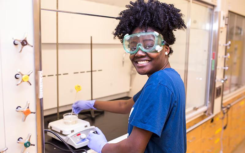 A student learns about the principles of Green Chemistry. A student wearing safety goggles