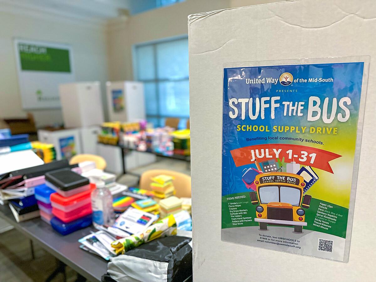 A sign for "Stuff the Bus" next to a table full of school supplies.