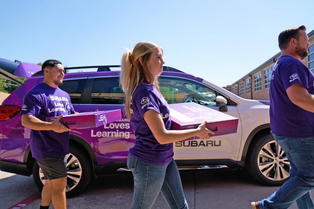 Three adults carrying boxes that say "Subaru Loves Learning"