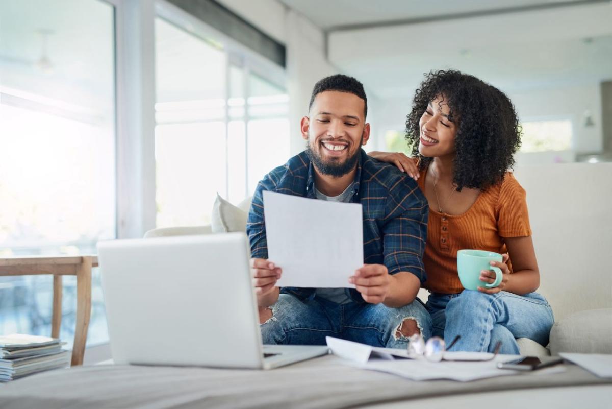 Smiling couple sitting on couch and looking at a piece of paper together