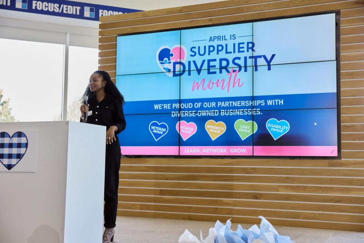 Woman speaking at a lectern in front of a sign reading, Supplier Diversity Month