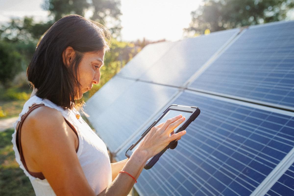 Woman holding a tablet and standing in front of a solar panel array.