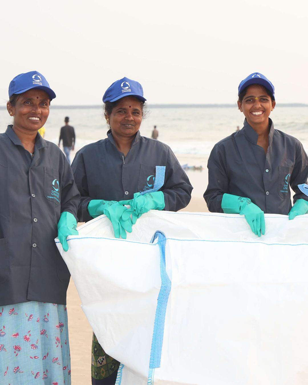 Three people on a beach with plastic gloves and a large container