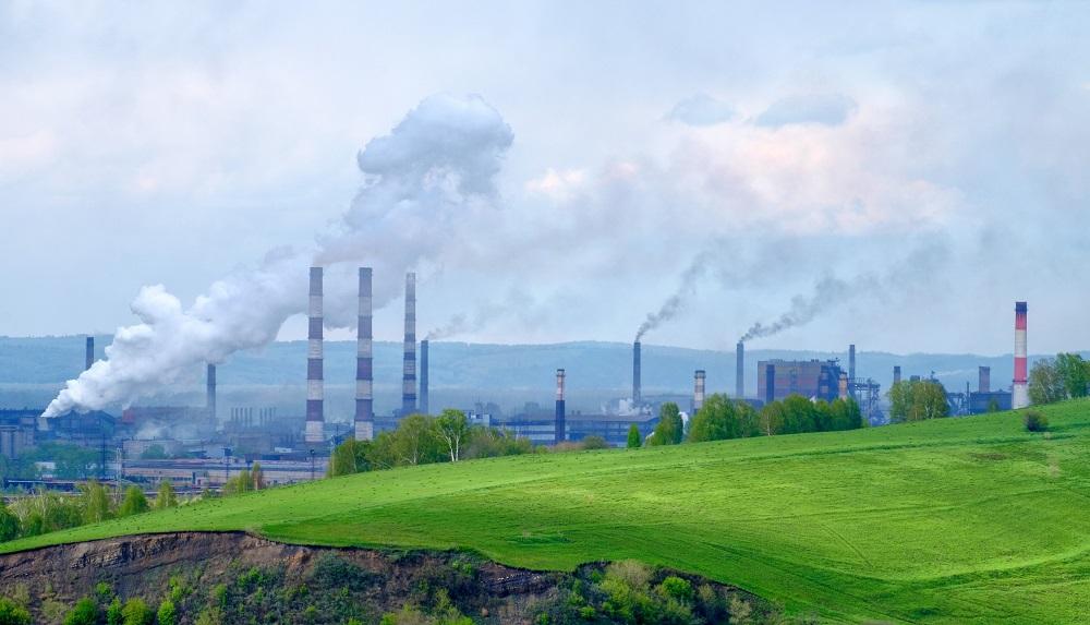 A grassy hill with many smoke stacks looming behind it