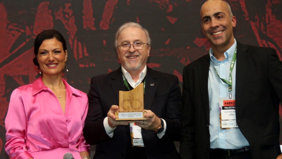 Vilmar Fistarol receives a 2022 AB Award for CNH Industrial’s innovations three people with the person in the center holding an award trophy