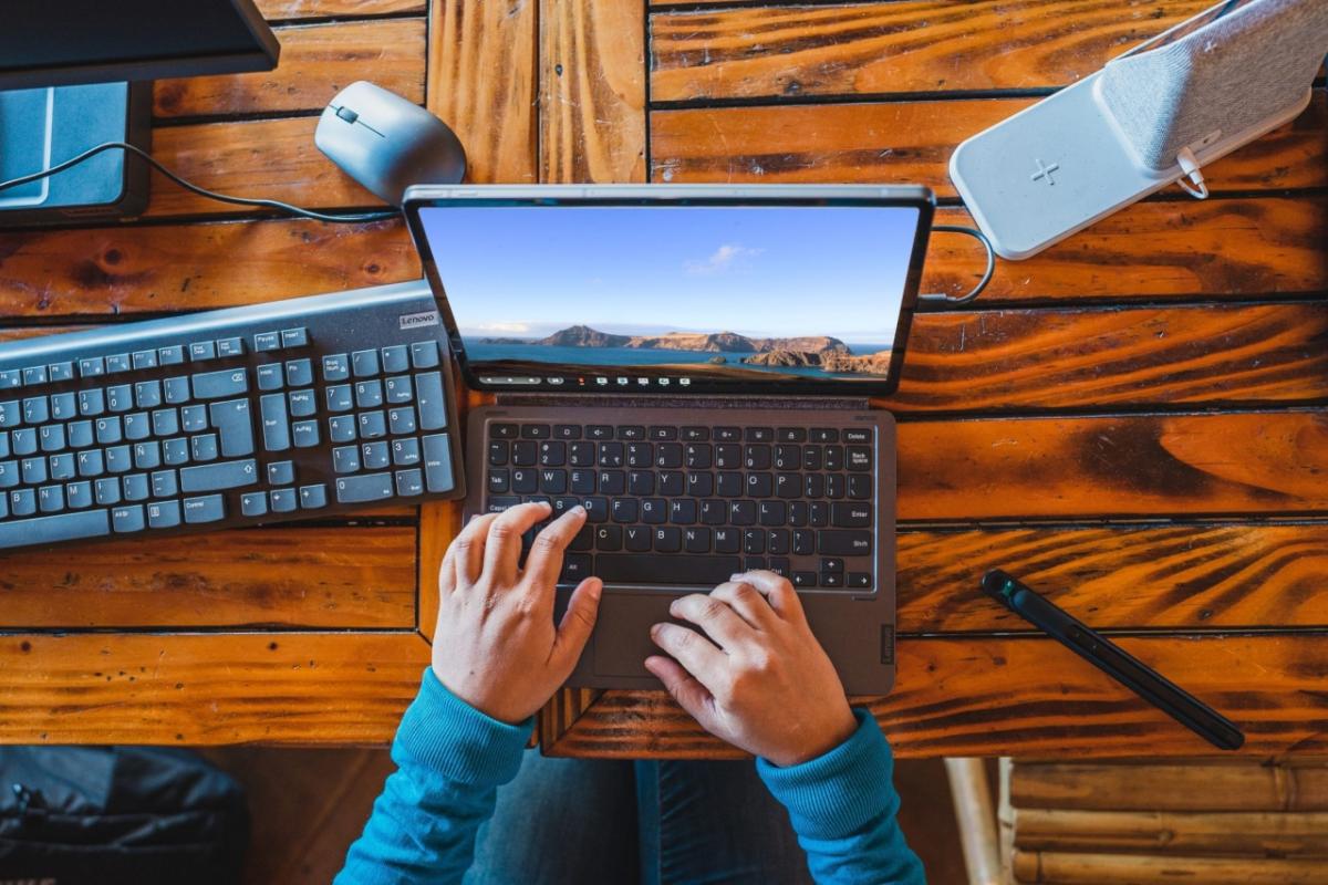 A pair of hands working on a laptop on a wooden table