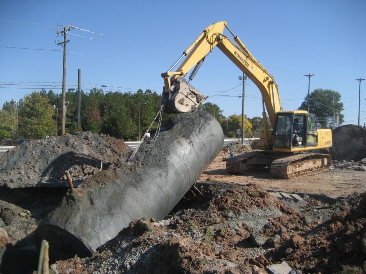 A yellow construction vehicle pulls a corroded UST out of the ground.