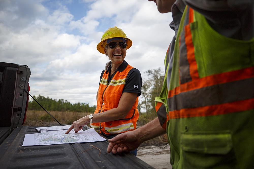 Terri Hall points to a map laid on the tailgate of a truck, smiling at another crew member