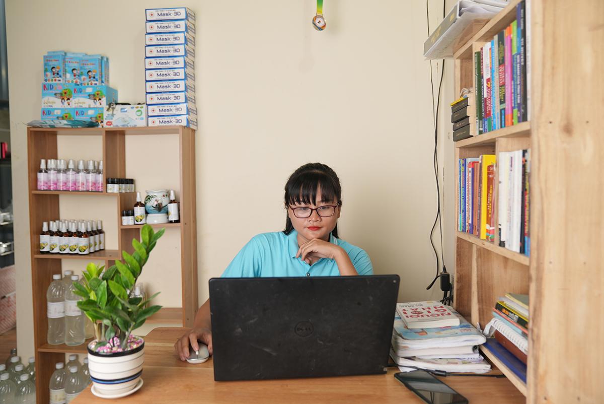 Thao sitting at a desk with a laptop. Shelves of books and products around her.