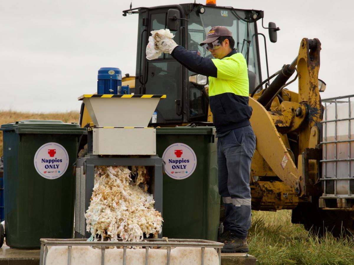 A person loading diapers into a bin with stickers 'nappies only.'