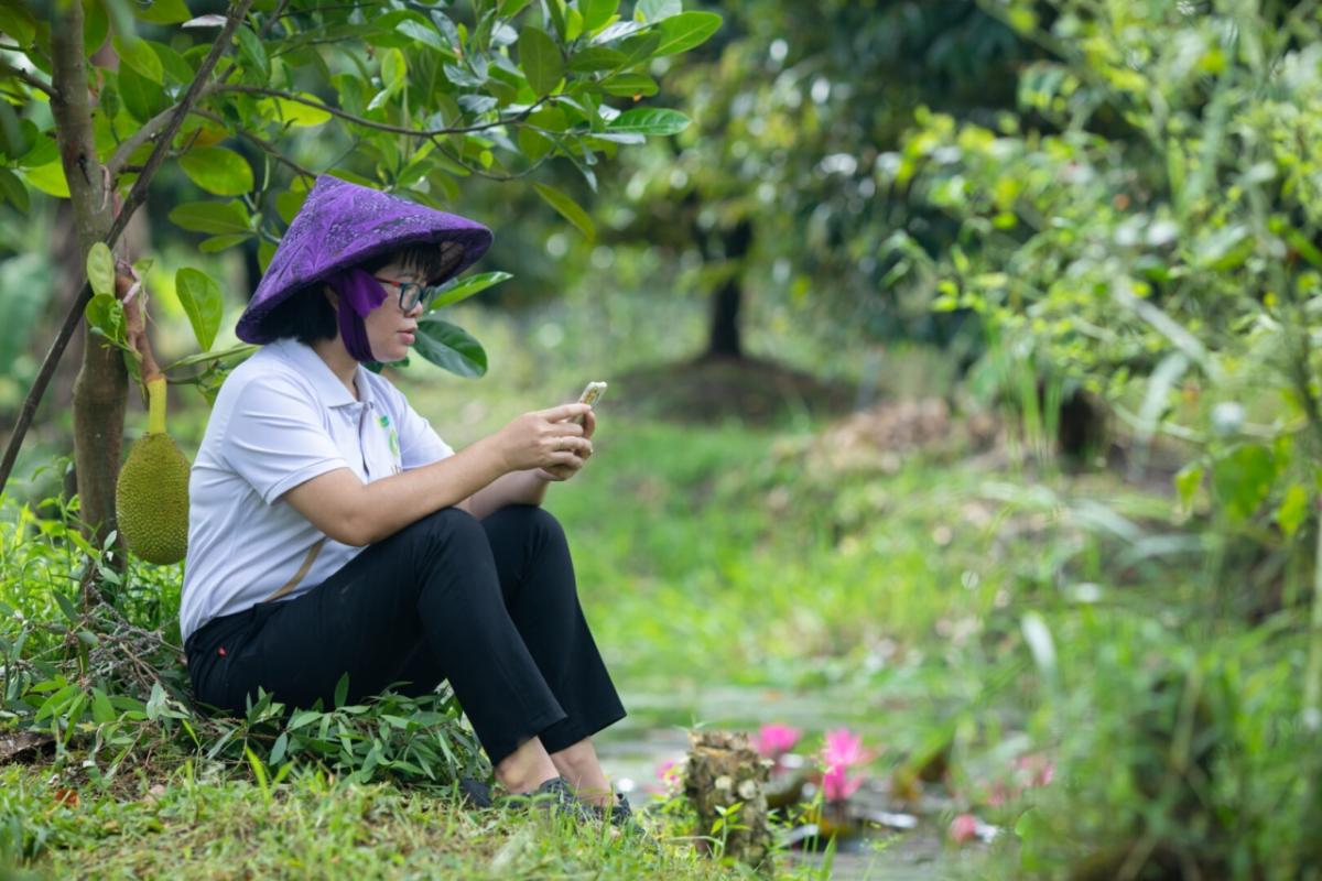 Thoa Nguyen sitting in an orchard using a cell phone.