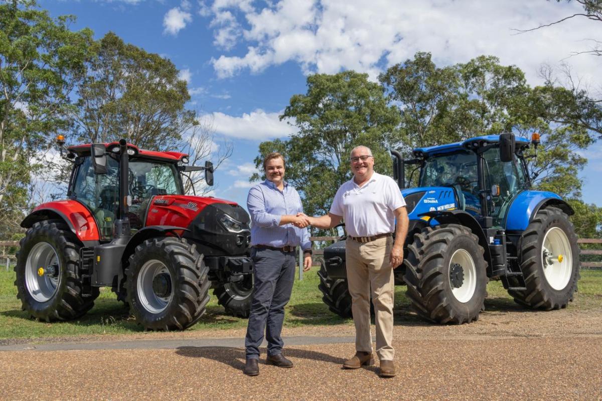 Two people shaking hands in front of two farming tractors outside.