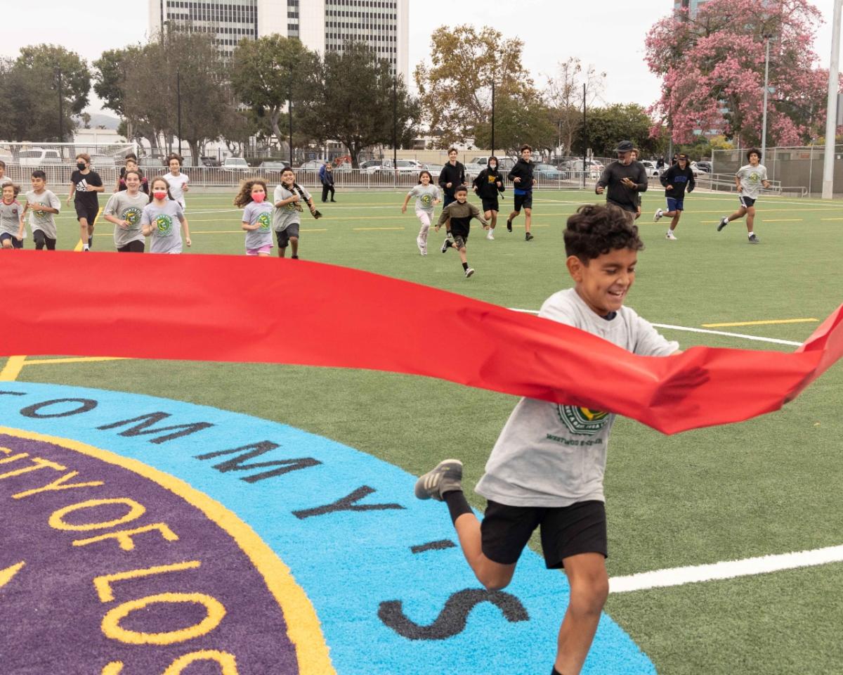 Local soccer youth fun through the red ribbon at centerfield of "Tommy's Field" to declare the pitch open to the public. 