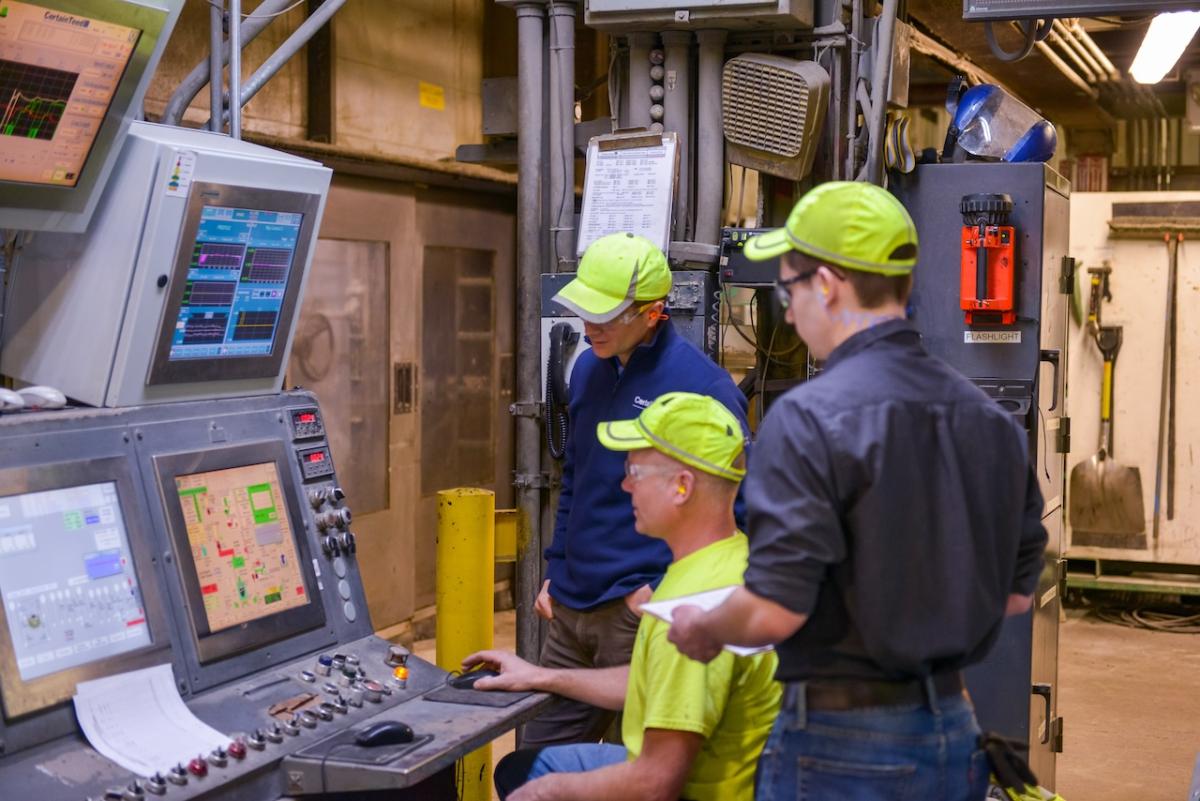 Three people working on a console in a warehouse.