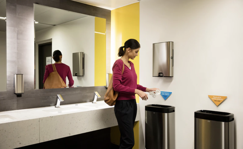 A woman standing in a bathroom using a paper towel.