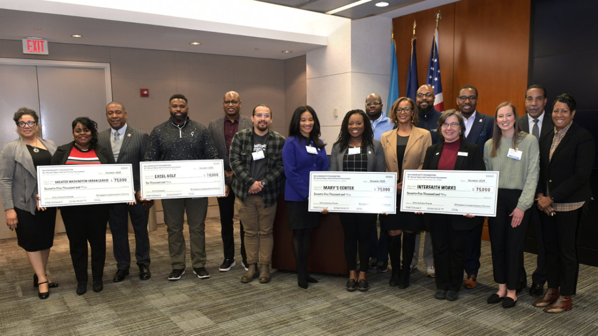 A group posed holding four large checks.