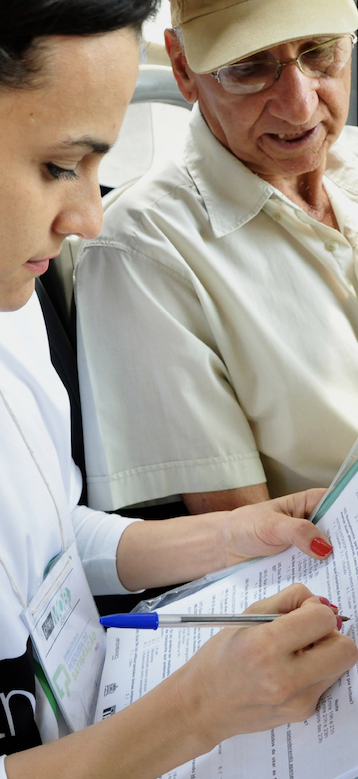 One person writing on a piece of paper with another person stood next to them looking over