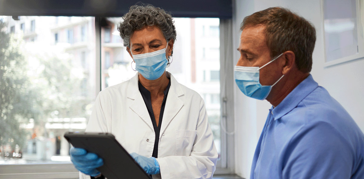 Healthcare professional and another person wearing face masks while looking at a tablet pc