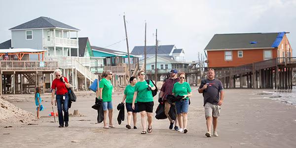A group of people, some in matching shirts, walking on a beach with trash bags.