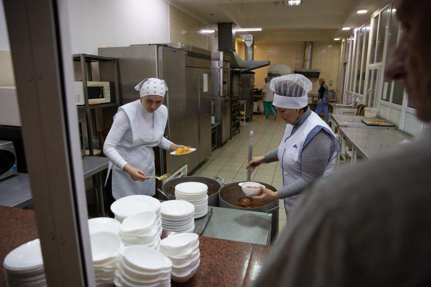 two people serving food from a kitchen