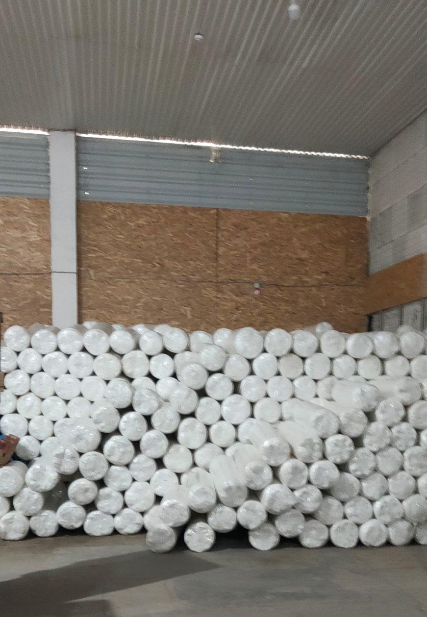 inside a small warehouse, wrapped and rolled mattresses stacked.