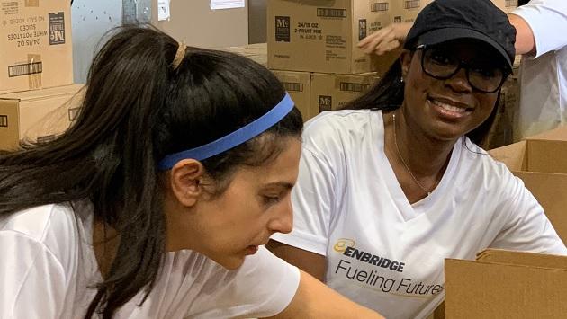 Enbridge employees Mayra, left, and Sonya help to package food hampers at Houston’s Target Hunger warehouse. Volunteers packing boxes, wearing "Enbridge Fueling Futures" t-shirts.