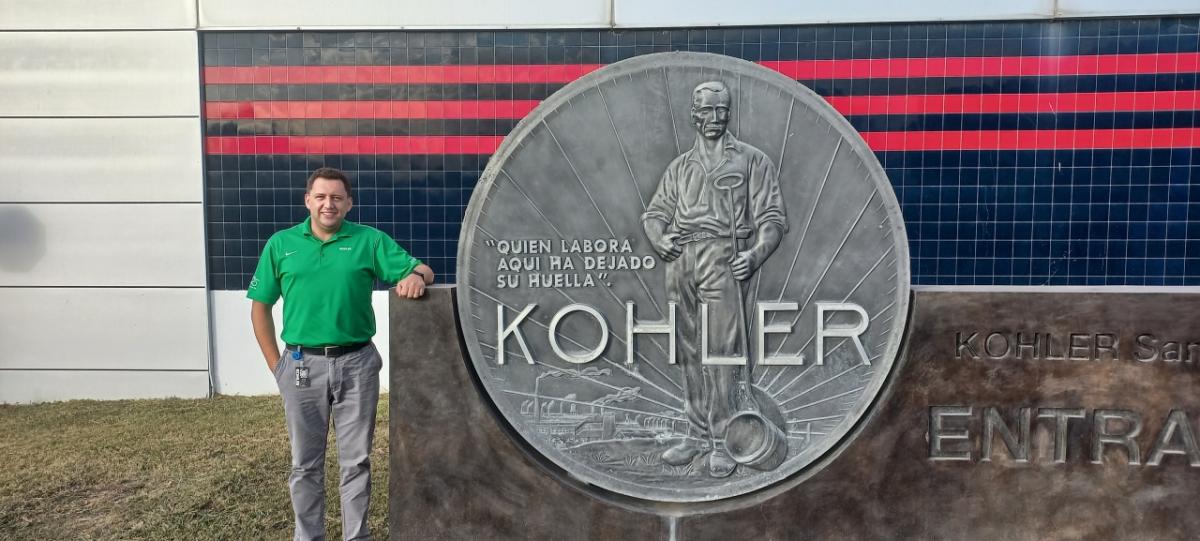 Vitor Wojastyk standing next to a large sign at the entrance of the Kohler plant