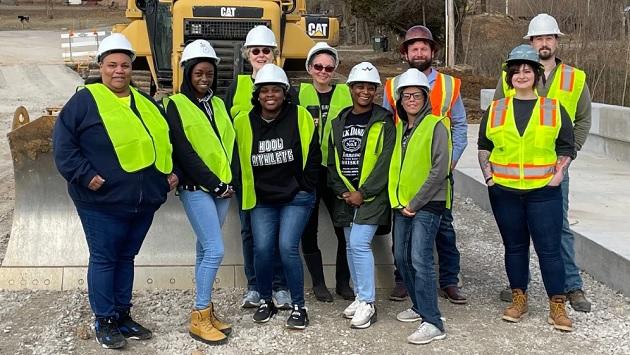 A group of people, in high-vis vests and hard-hats, posed in front of construction machinery.