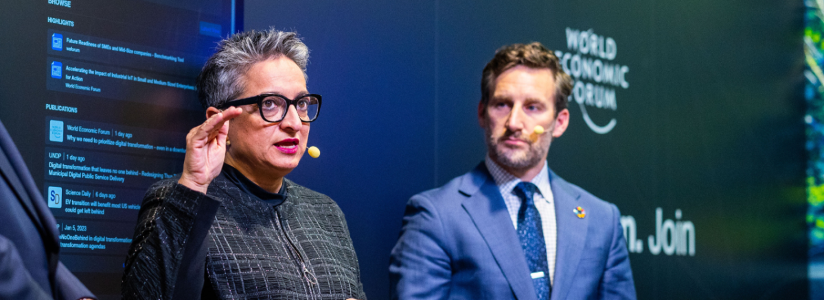 Close-up of two speakers, one looks at the other, both wearing headset microphones. 