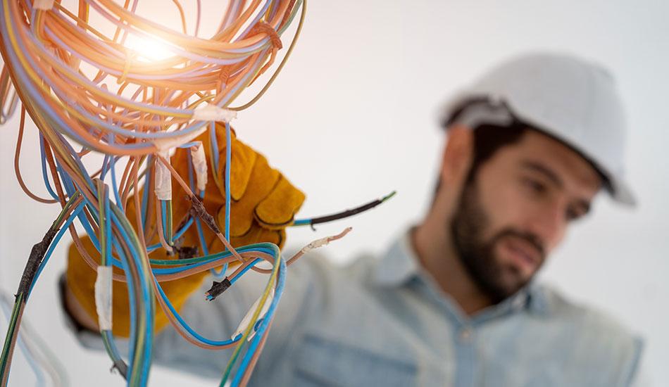 Electrical worker shown wearing a helmet and working on wiring.