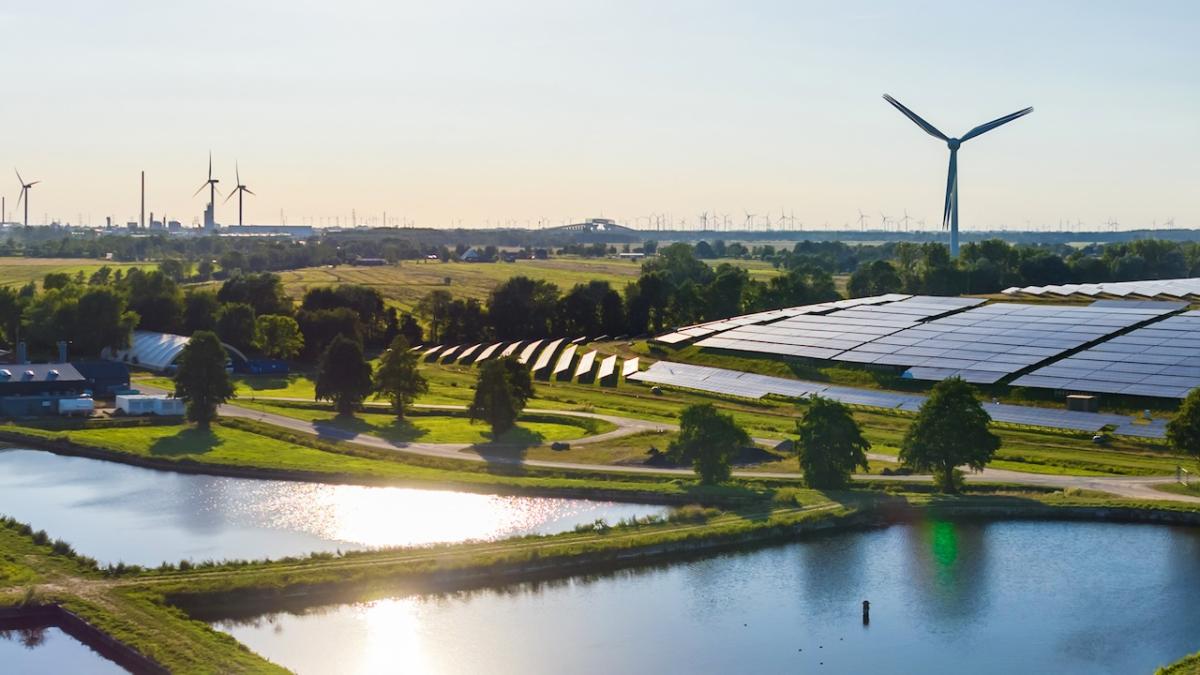 Windmill and solar panel farm shown with a water source in the foreground.