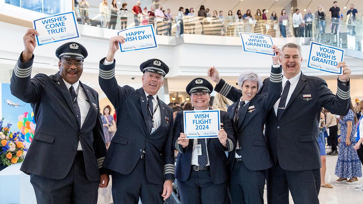 Five cheering pilots holding signs in an airport "Wishes come true" "Happy Wish Day" and "Wish flight 2024."