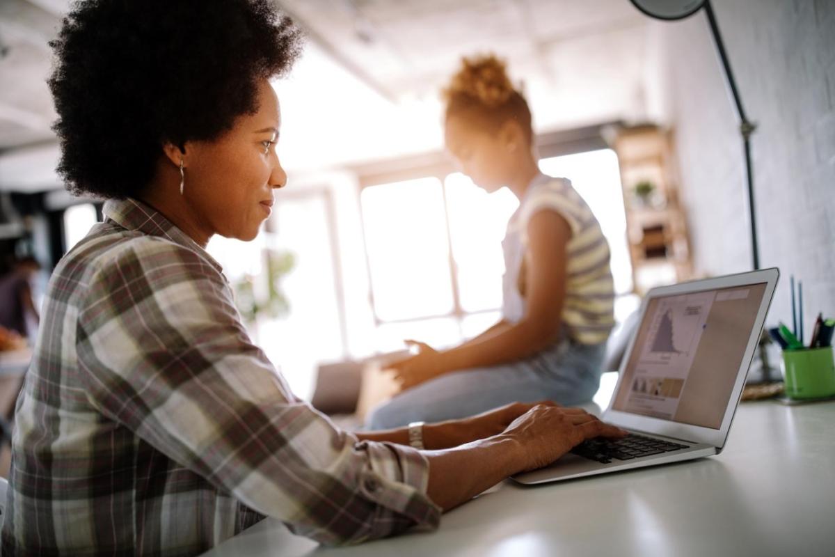 woman working on a laptop with a child in the background