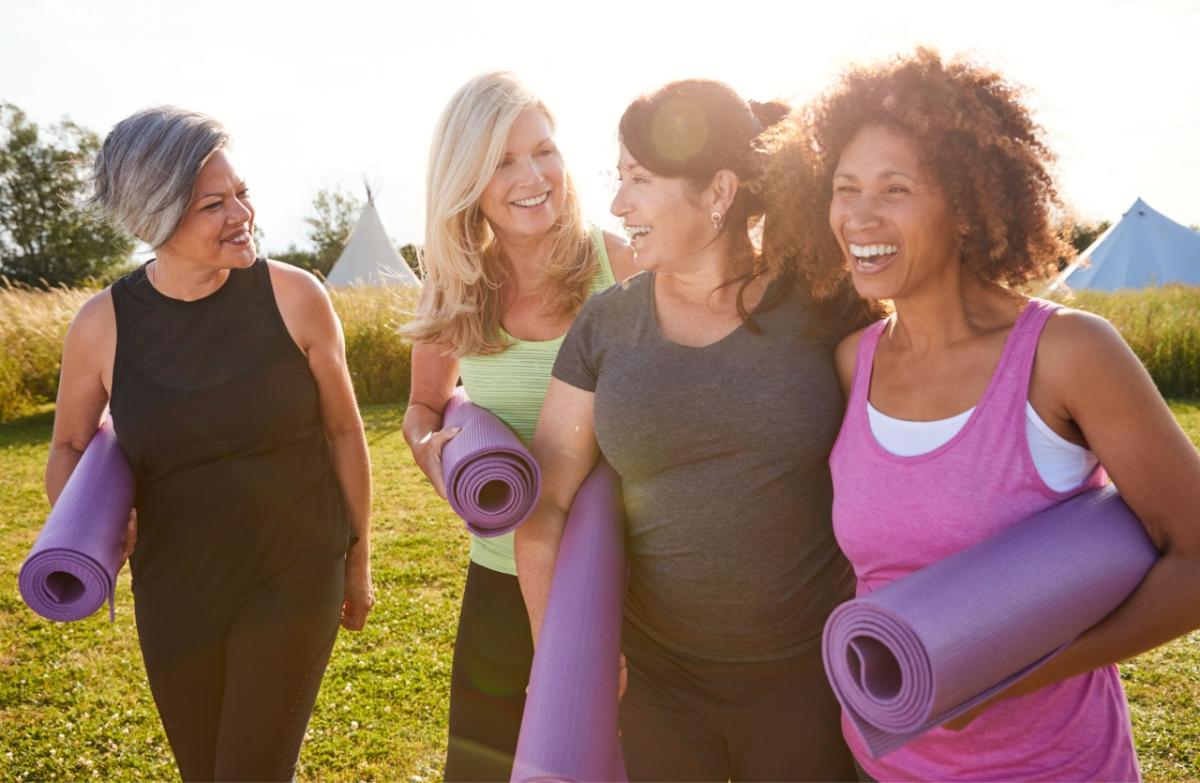 A photo of 4 women walking through a field holding yoga mats under their arms