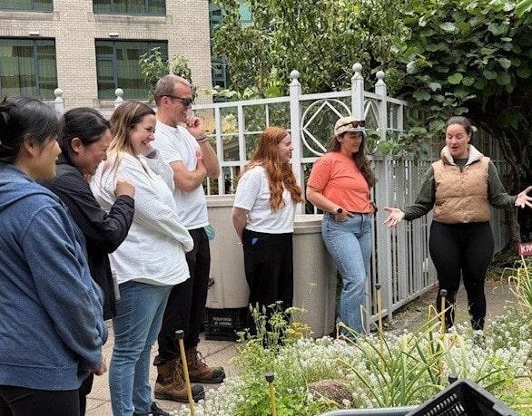 DP World volunteers gathered on the YWCA Rooftop Garden as an instructor explains the day’s tasks, surrounded by raised beds and greenery.