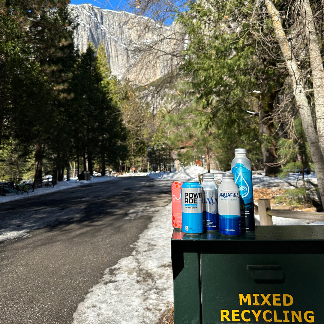 Recyclable bottoms on top of a mixed recycling bin. In the background are mountains and trees.