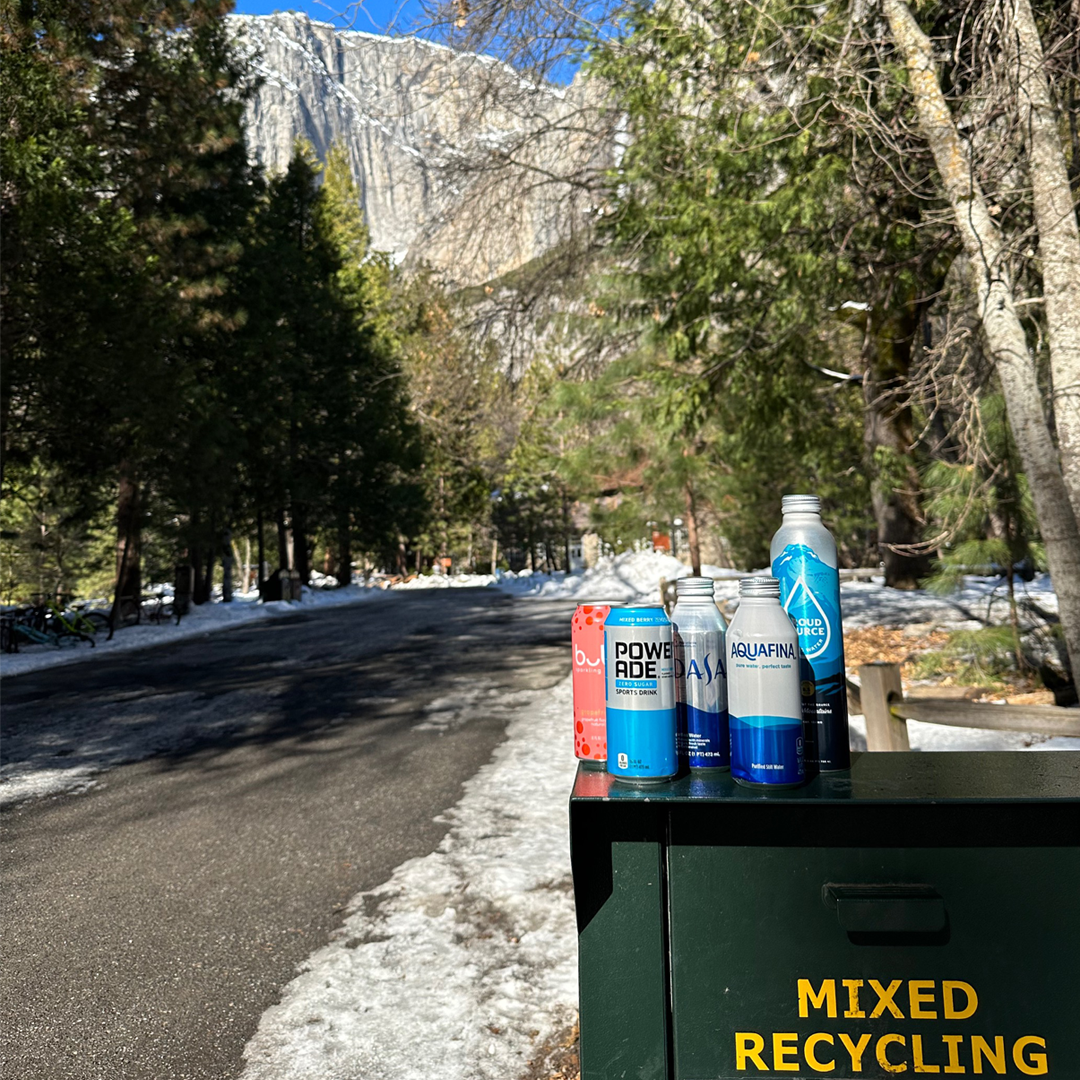 Recyclable bottoms on top of a mixed recycling bin. In the background are mountains and trees. 