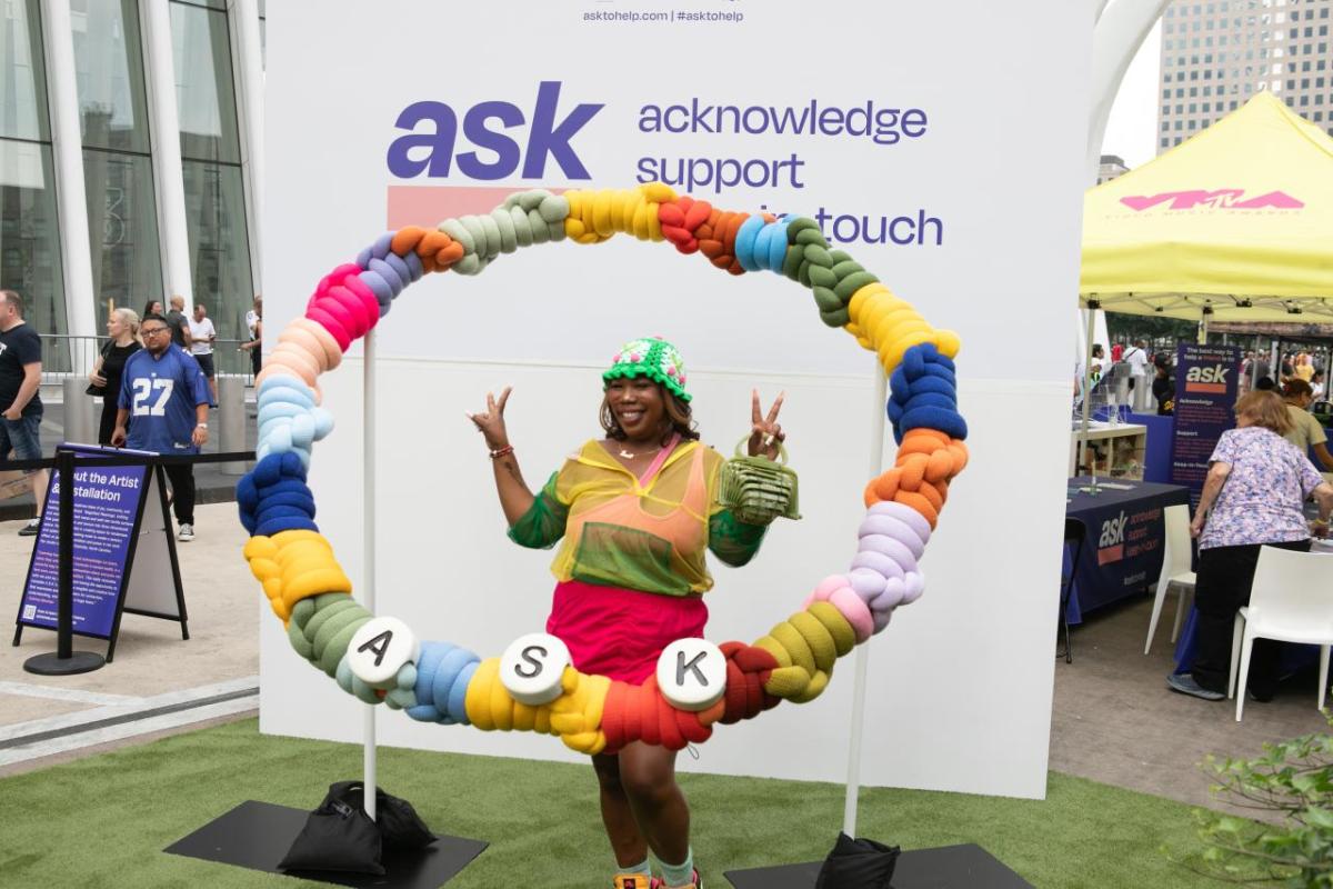 woman holding up peace signs in a giant friendship bracelet with the word "ASK"