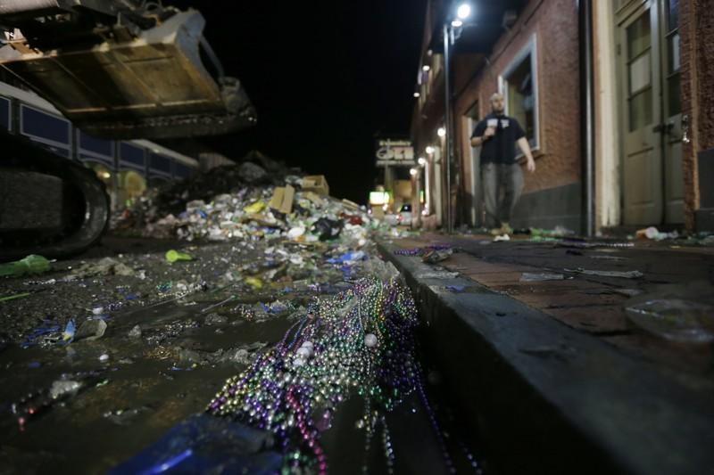 FILE - In this Feb. 13, 2013 file photo, people walk past debris debris on Bourbon Street in the early morning of Ash Wednesday, the day after Mardi Gras, in the French Quarter of New Orleans. Mardi Gras produces fun-filled days of merriment, joy and the occasional hangover. It also produces a lot of garbage. But this year two New Orleans organizations aimed to change that with a pilot recycling project to collect cans, plastic bottles and that Mardi Gras accessory found hanging on fences, trees, and balconies: beads. (AP Photo/Gerald Herbert)
