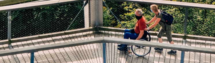 a person pushing another in a wheelchair across a bridge