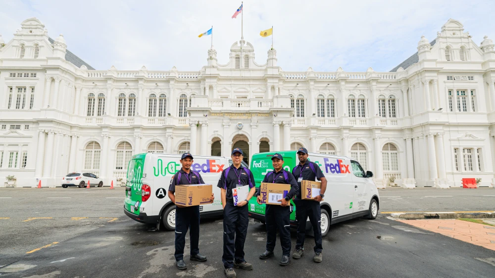 FedEx employees holding packages, next to vehicles