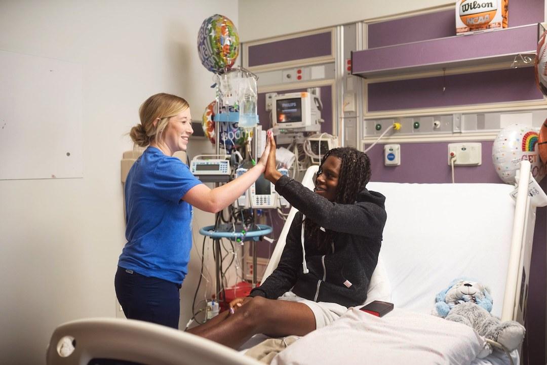 Patient sitting in a bed giving a high five to a nurse.
