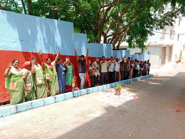 A line of people raising their hands and smiling, against a red and white wall