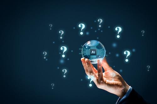 Image courtesy of eSchool News A hand holding a clear ball with "AI" and surrounding "?"s digitally imposed, on a dark background.