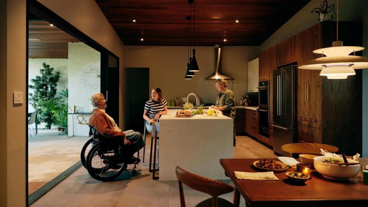 A person in a wheelchair talking with two others at a kitchen island.