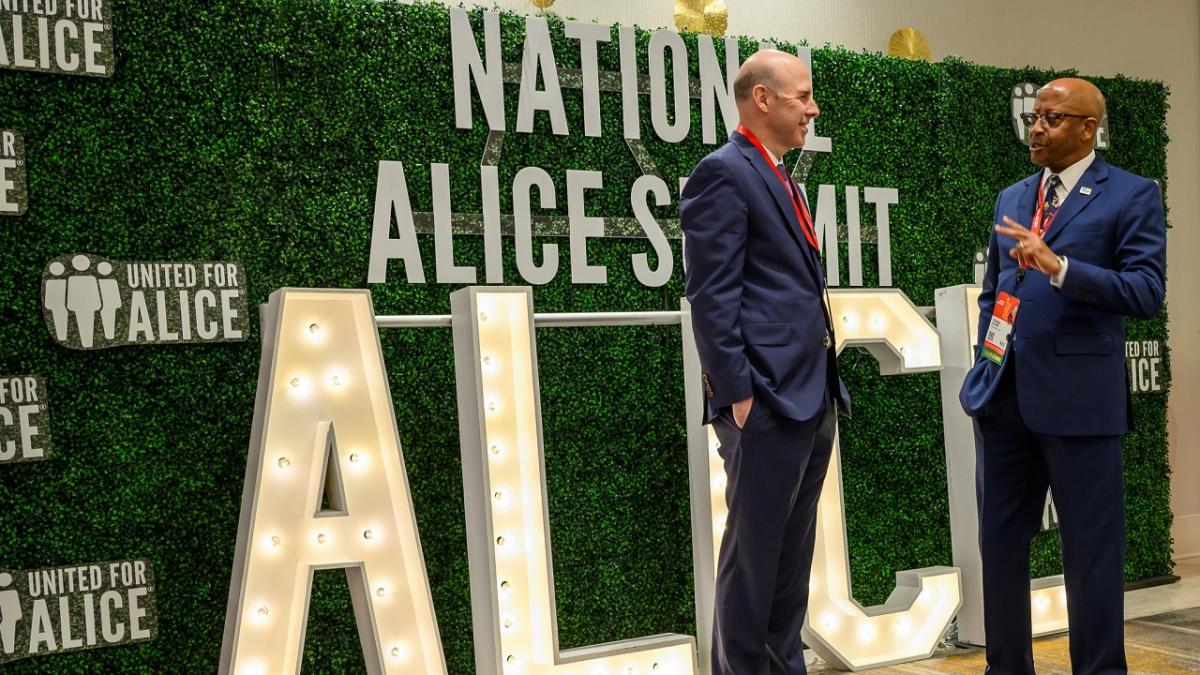 Two people talking in front of "National ALICE Summit" sign.