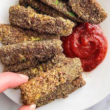 a hand picks up a 'zucchini fry', a red dipping sauce on the side