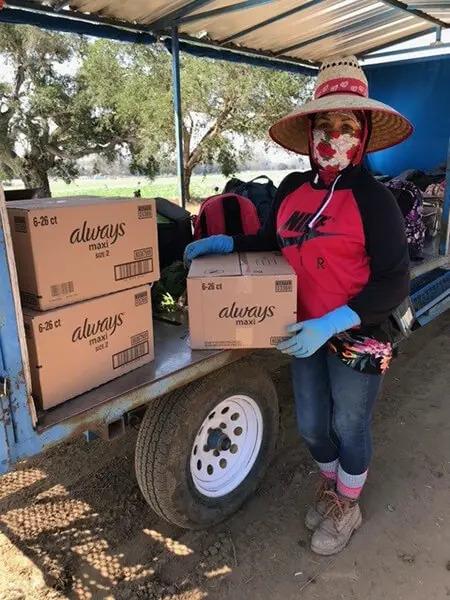 A worker holding a box with "always" logo, other boxes on an open cart next to them