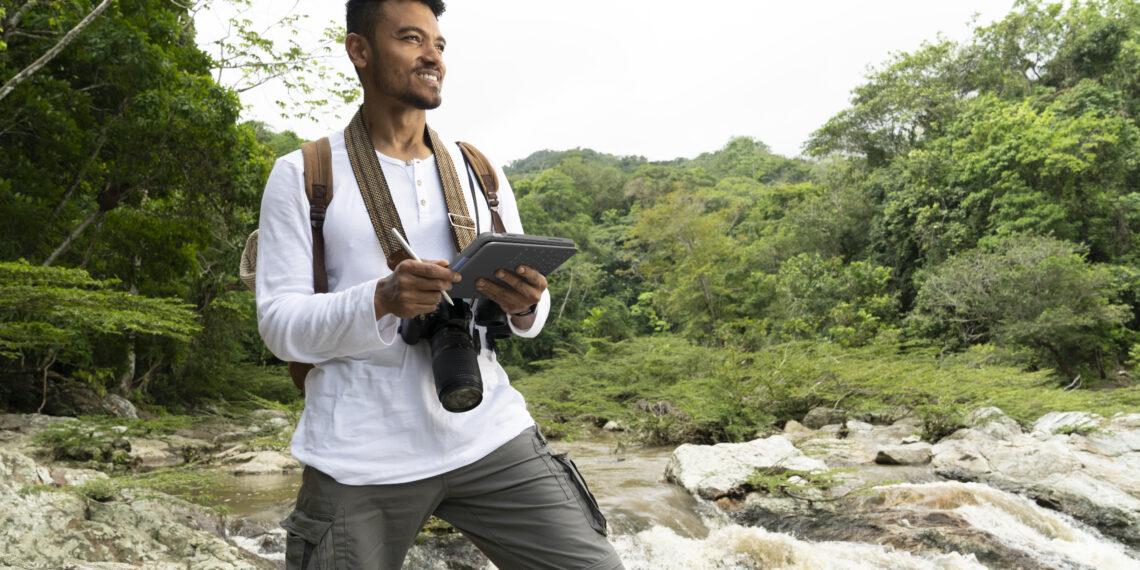 A smiling person with a camera and notepad next to a stream