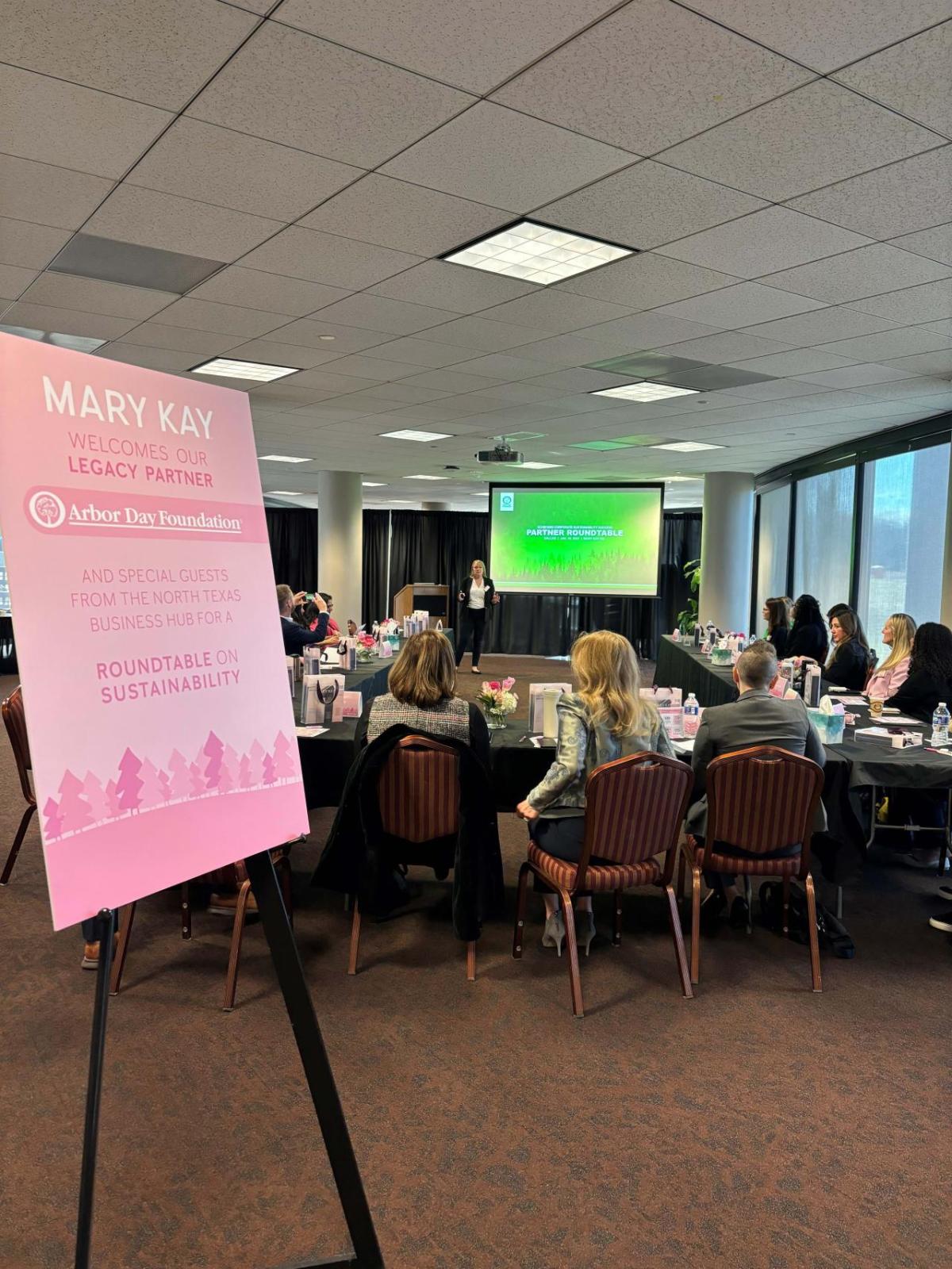 People seated in a conference room a sign "Mary Kay welcomes our legacy partner Arbor Day Foundation."